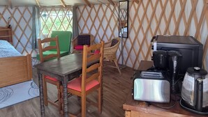 Ein gemütliches Zeltinnere mit Holztisch, Stühlen, einem Bett und einer Küchenzeile.