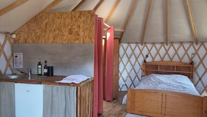 Eine Jurte mit Holzinnenraum, einem Bett, einer kleinen Küchenzeile und einem Fenster.