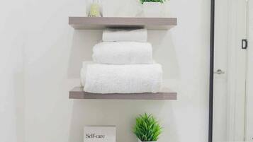 Un baño con un estante de madera que sostiene toallas blancas, una pequeña planta en maceta y un cartel con la palabra 'Self-care' y una definición.