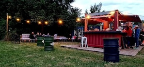 Un área de bar al aire libre con asientos, luces colgantes y una terraza de madera.