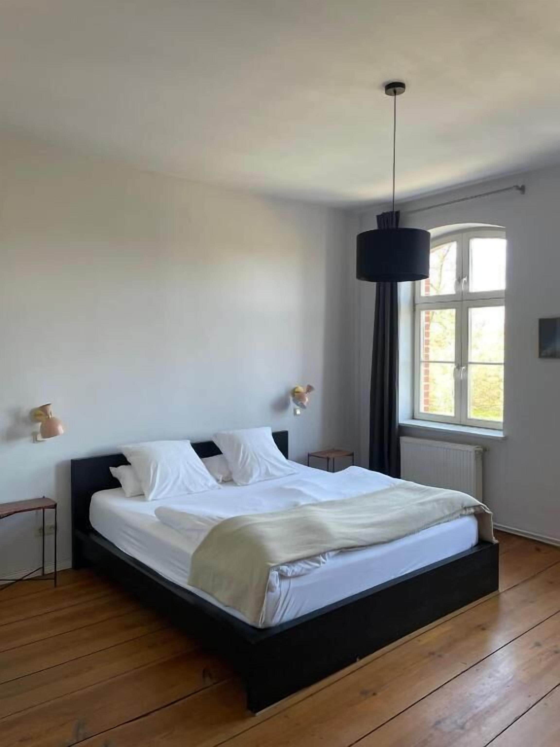 Ein Schlafzimmer mit Bett, einer Pendelleuchte, einem Fenster und einer Heizkörper.