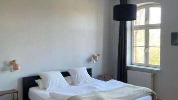 Ein Schlafzimmer mit Bett, einer Pendelleuchte, einem Fenster und einer Heizkörper.