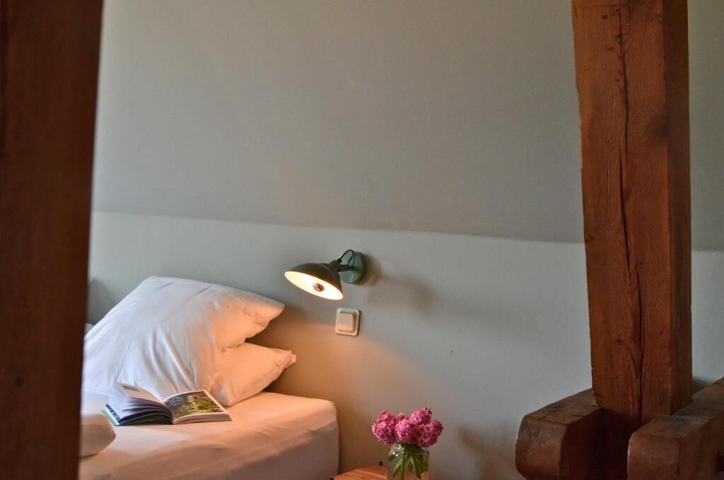 Ein Bett, ein Buch, eine Wandlampe und eine Vase mit Blumen.