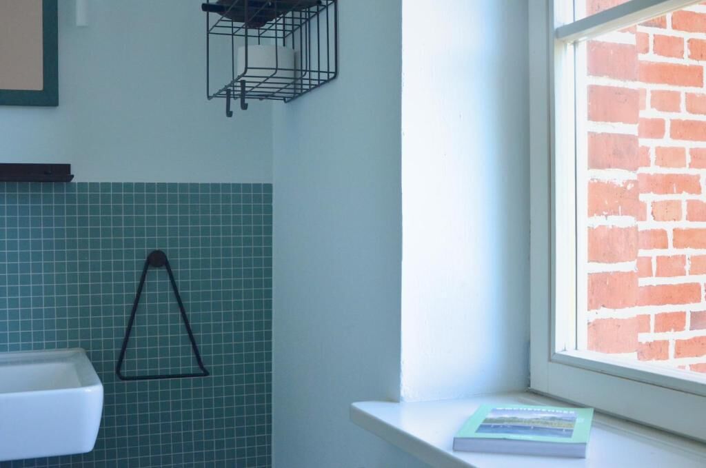 A bathroom with a tiled wall, a black triangular towel rack, a white sink, and a window with a brick wall view.