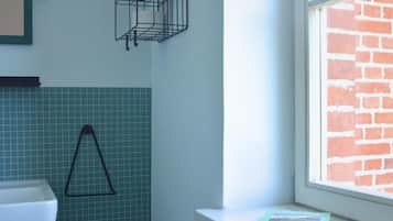 A bathroom with a tiled wall, a black triangular towel rack, a white sink, and a window with a brick wall view.