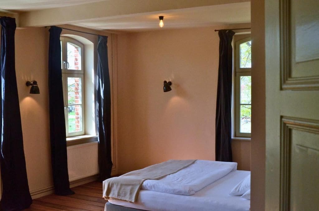 A bedroom with a bed, two windows, and wall-mounted lamps.
