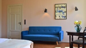 A room with a blue sofa, a white door, a framed poster on the wall, and a small table with a vase of flowers. - An den Wiesen. Gasthaus am Finowkanal (Wandlitz)
