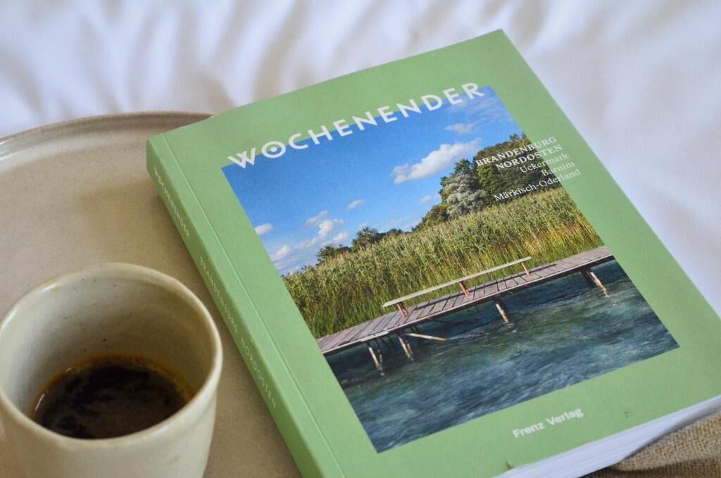 A book titled 'WOCHENENDER' with a cover image of a bridge over water, placed next to a cup of coffee on a tray.