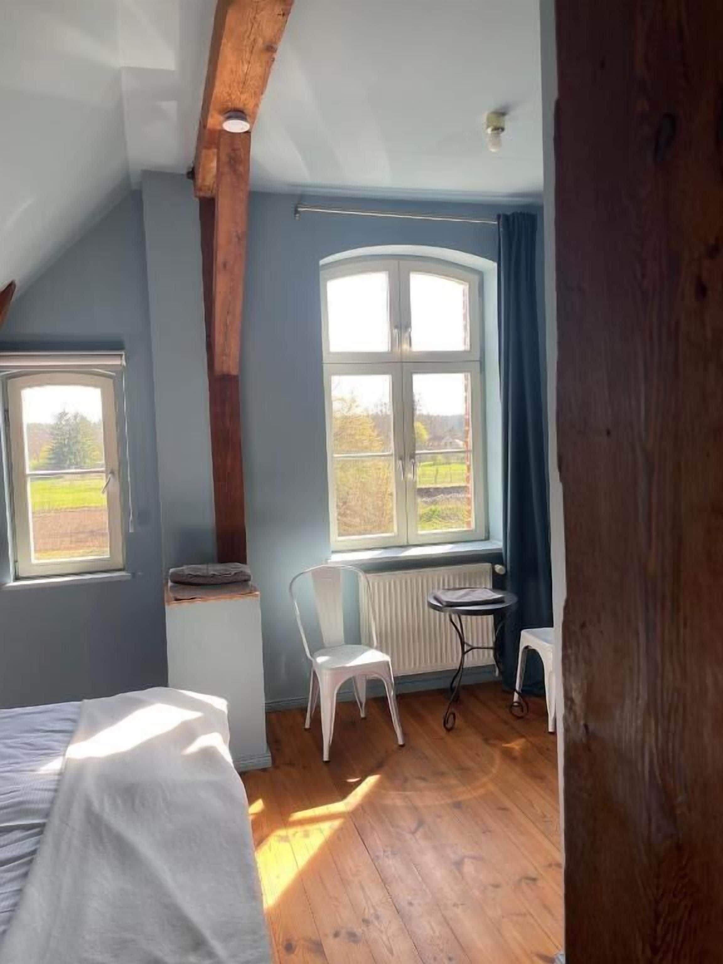 Ein Zimmer mit Bett, Stuhl, Tisch und Fenster.