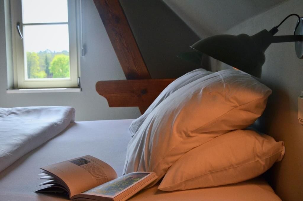 Un dormitorio con cama, ventana y lámpara de lectura.