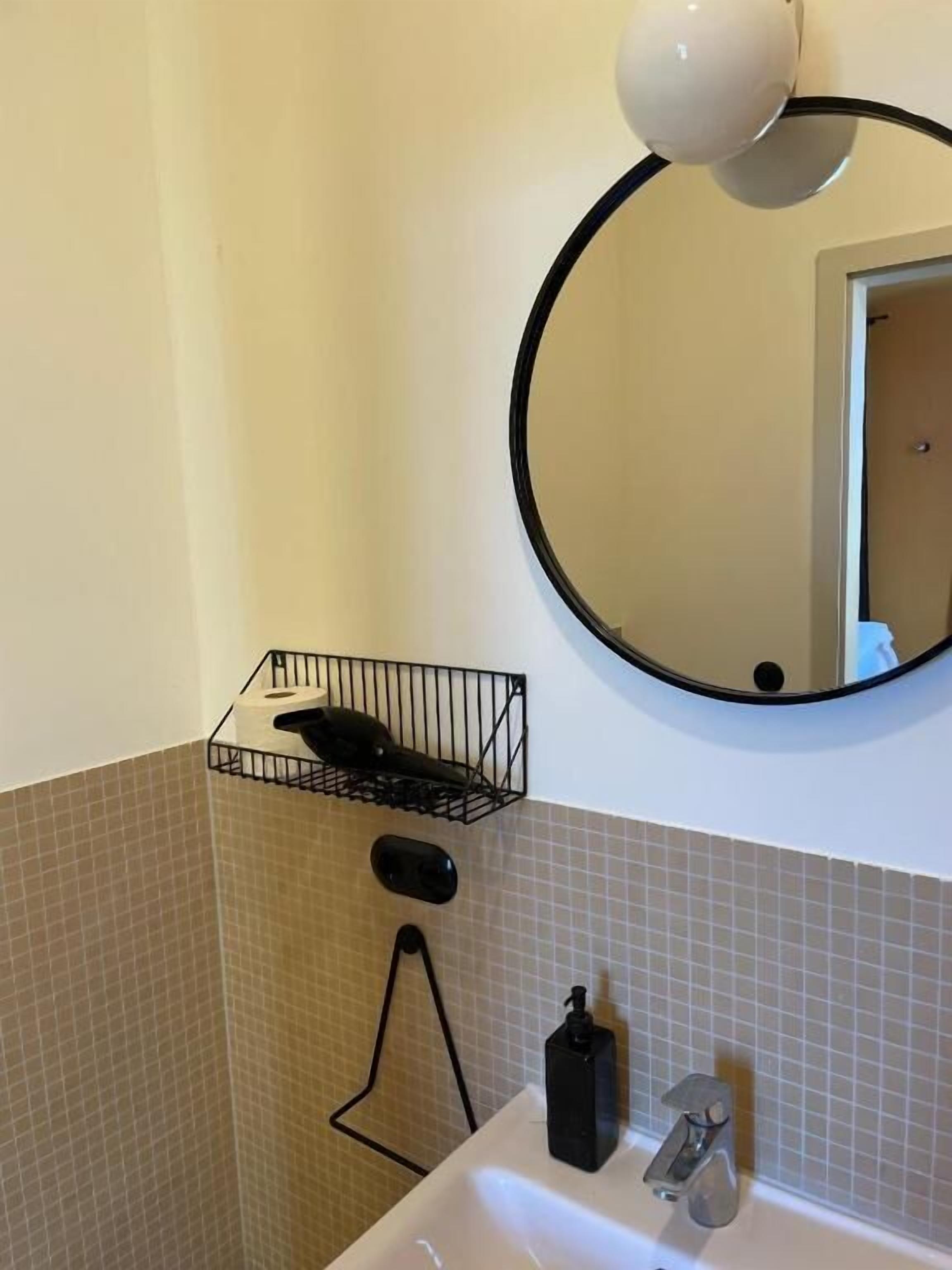 Ein Badezimmer mit rundem Spiegel, schwarzem Seifenspender und Handtuchhalter.