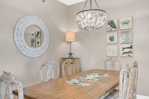A dining room with a wooden table, chairs, a chandelier, wall art, and a lamp. - One Particular Harbour Lagoon View 391-203 · Pet-Friendly (Bradenton)