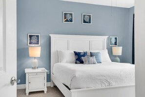 Un dormitorio con una cama blanca, dos mesitas de noche con lámparas, y tres cuadros en la pared.