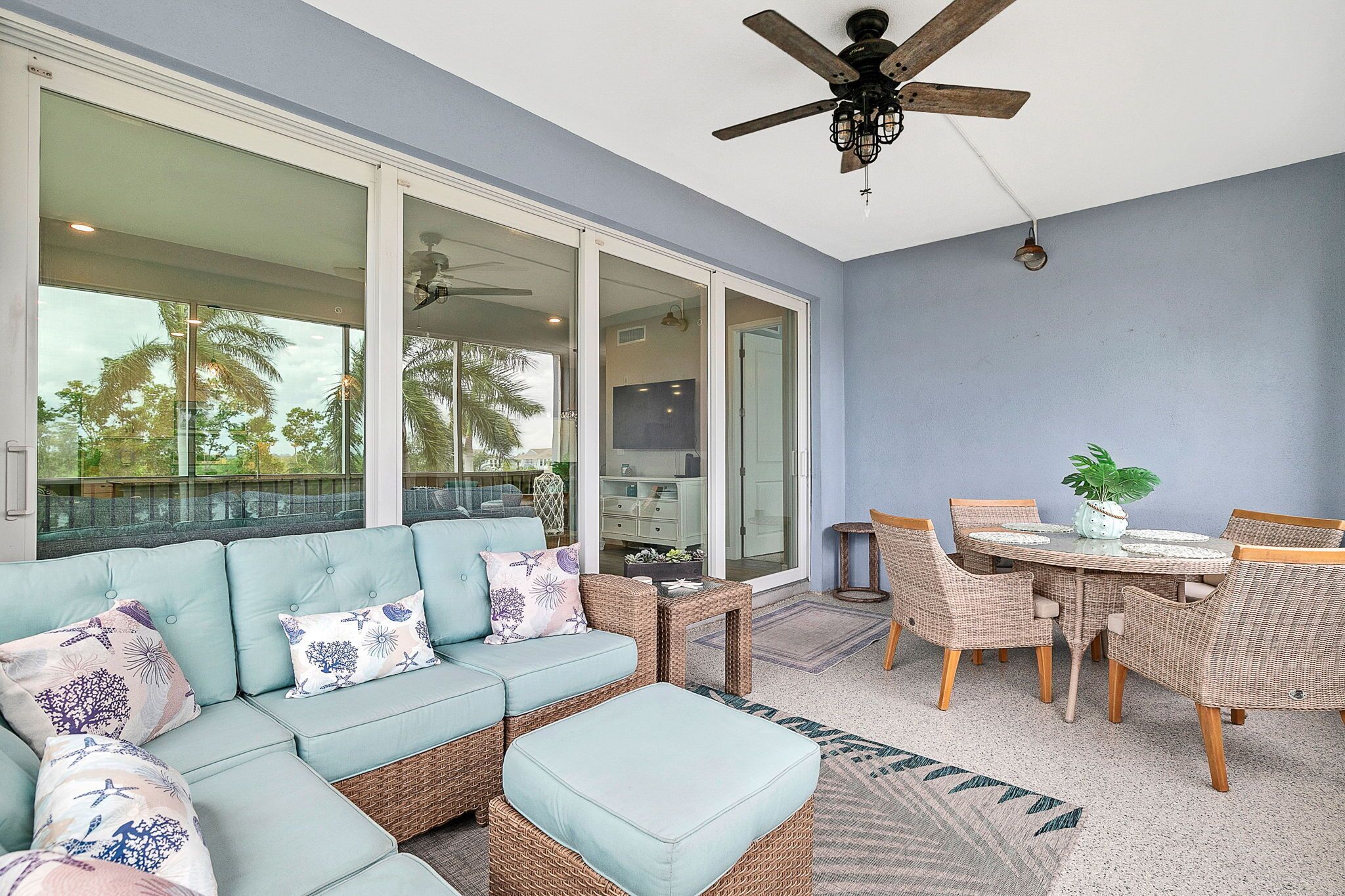 A sunlit room with a light blue sofa, wicker chairs, a dining table, and a ceiling fan.