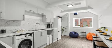 Una cocina moderna con lavadora, armarios blancos y un comedor con mesas de madera.