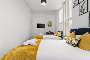 Habitación de hotel con dos camas, televisión y ventana con luz natural.