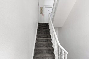 Una escalera con barandilla blanca y peldaños alfombrados que conduce a una puerta marcada con el número 2.