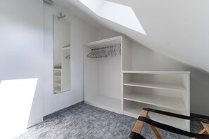 Ein Zimmer mit schrägem Dach, einem großen Spiegel und eingebauten Regalen.
