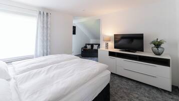 A hotel room with a bed, a TV, a desk, and a plant.