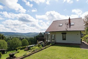 A single-story house with a tiled roof, a small porch, and a garden with a wooden bench.