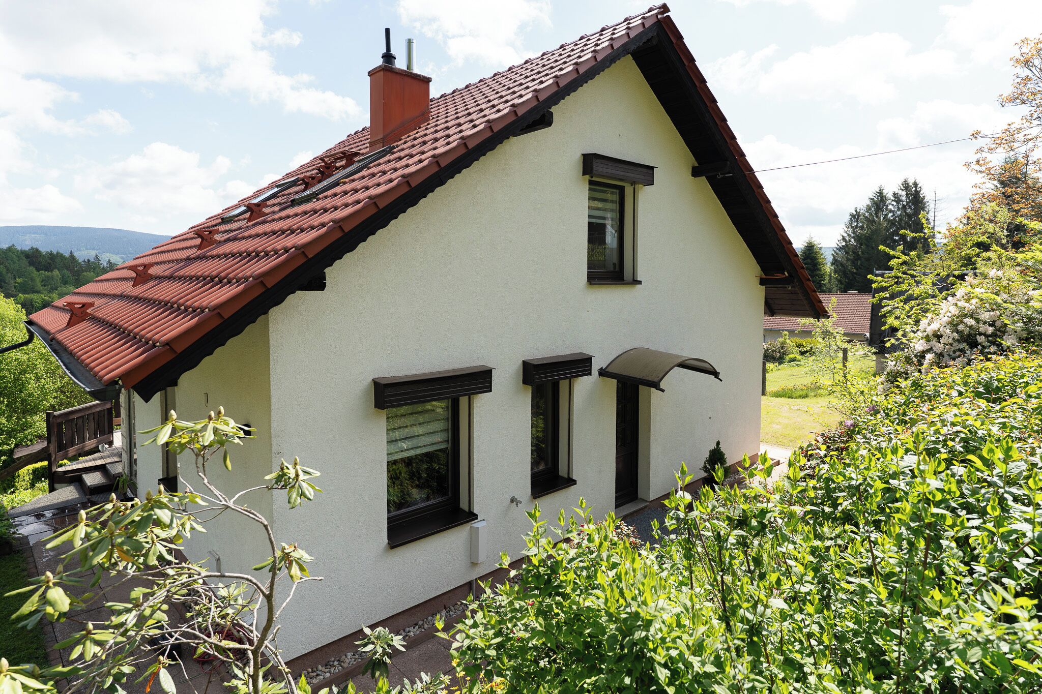 Ein zweistöckiges Haus mit rotem Ziegeldach, weißen Außenwänden und einem kleinen Garten mit verschiedenen Pflanzen.