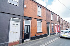 A row of terraced houses with distinct front doors and windows, a parked car, and a clear sky. - St Helens Stay | Ideal for Work & Short Stays (Warrington / St Helens)