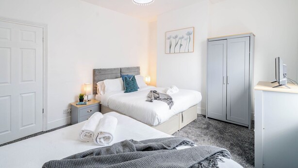 Una habitación de hotel con cama, mesitas de noche, un escritorio con computadora, armario y lámpara en el techo.