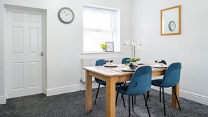 Un comedor con una mesa dispuesta para cuatro personas, un reloj en la pared y una ventana con persianas.