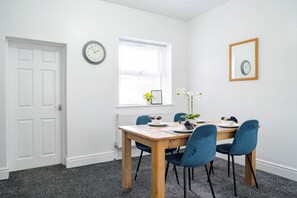 A dining area with a table set for four, a clock on the wall, and a window with blinds. - St Helens Stay | Ideal for Work & Short Stays (Warrington / St Helens)