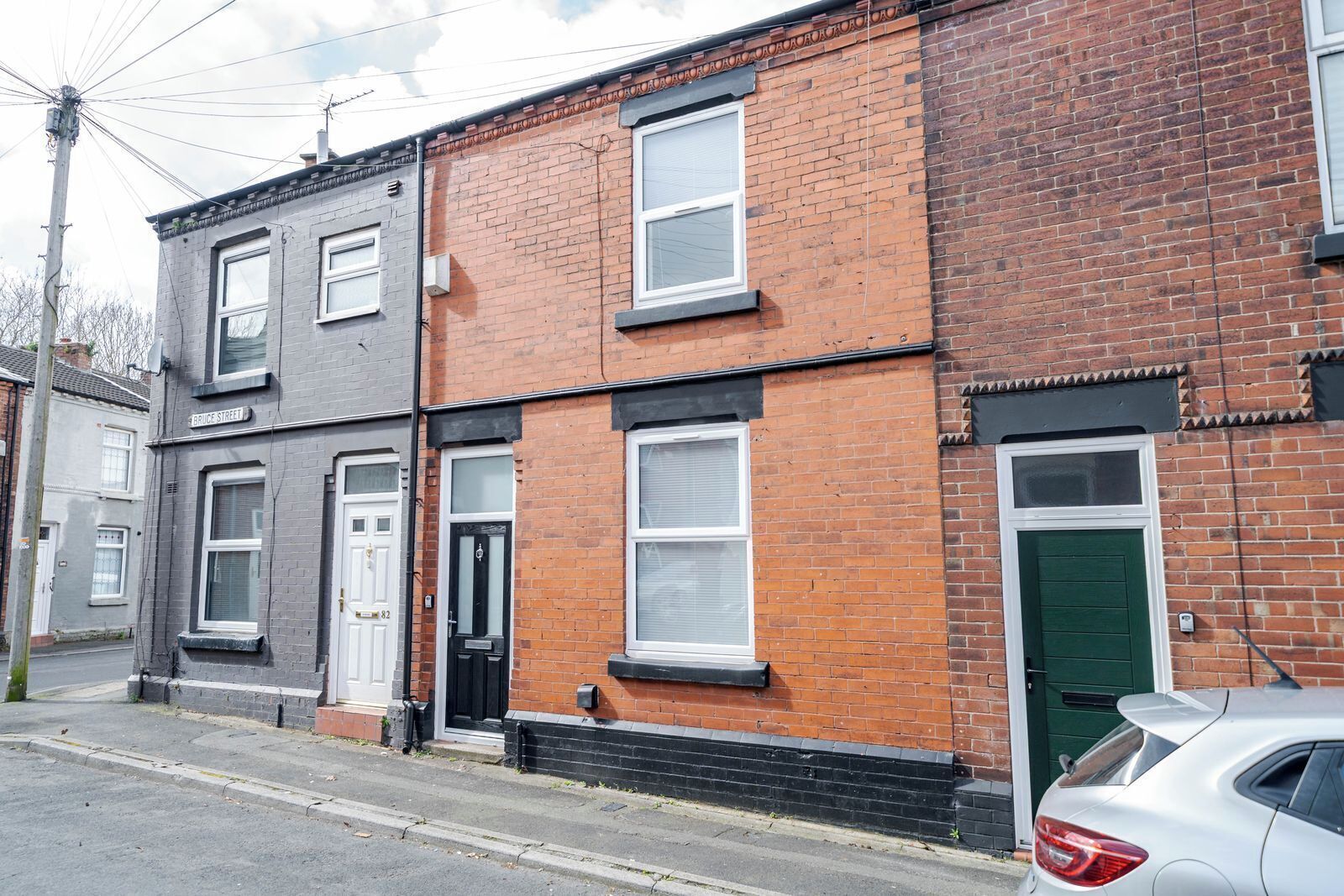 A row of terraced houses with distinct brick facades, a street, and a parked car.