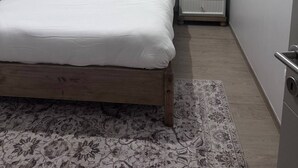 Siististi pedattu sänky valkoisilla lakanoiden kanssa, yöpöytä lampulla ja kuviollinen matto lattialla.