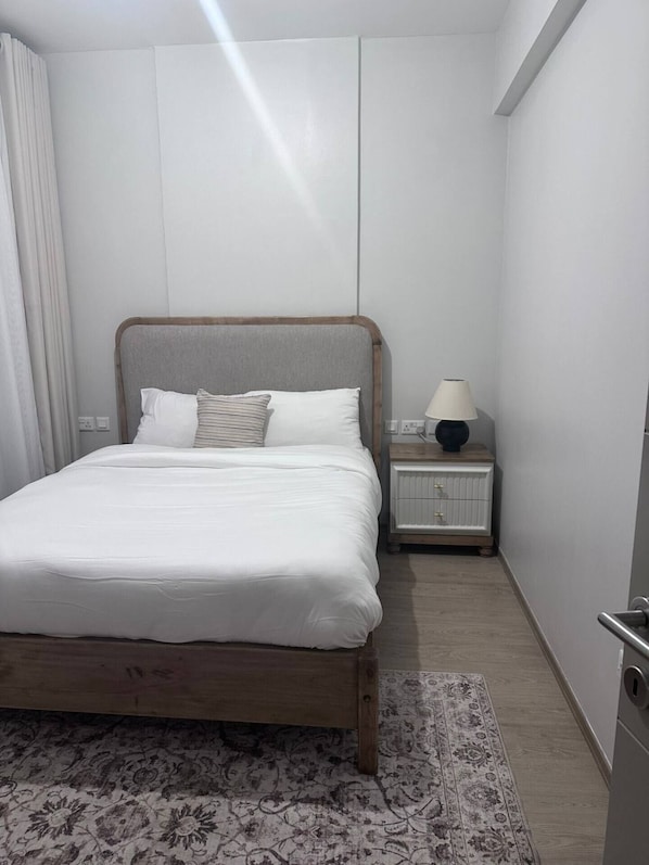 Un lit bien fait, avec du linge de lit blanc, une table de chevet avec une lampe et un tapis à motifs sur le sol.