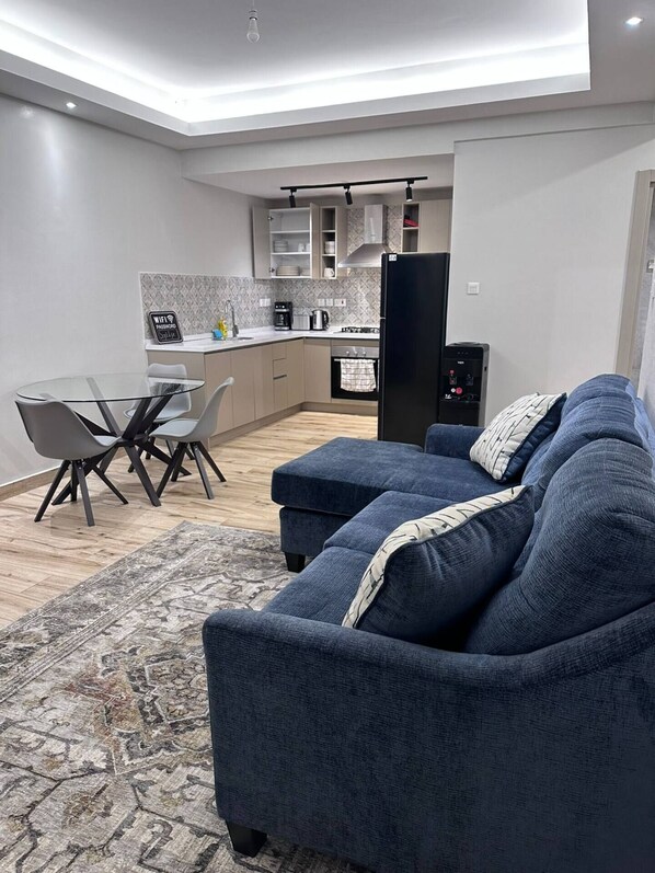 Ein moderner Wohnbereich mit Sofa, Esstisch und einer Küche im Hintergrund.