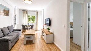 Ein modernes Wohnzimmer mit grauem Sofa, einem Holzesstisch und einem an der Wand montierten Fernseher.