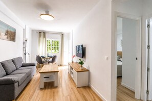 A modern living room with a grey sofa, wooden dining table, and a TV mounted on the wall. - 1021 Apartment Morasol (Nerja)