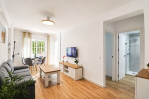 Una sala de estar moderna con sofá, mesa de comedor, televisor y zona de ducha con paredes de vidrio.