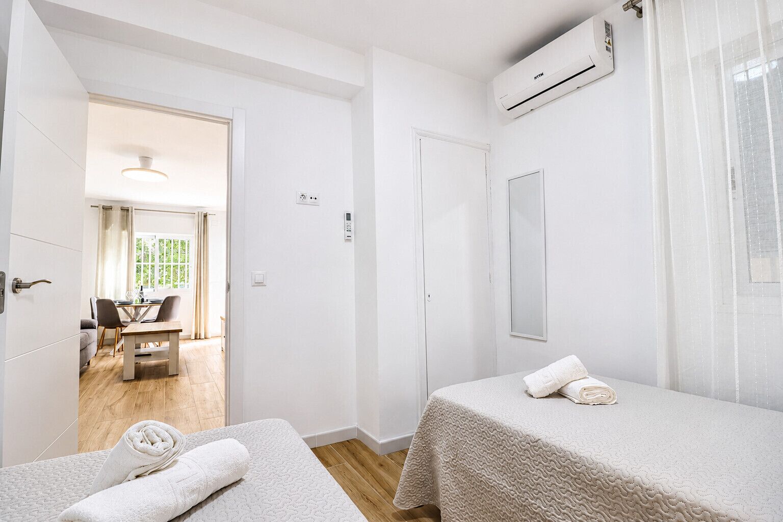 A hotel room with two beds, a dining area, and an air conditioning unit.