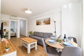 Una sala de estar moderna con un sofá, una mesa de comedor para dos personas y un televisor.