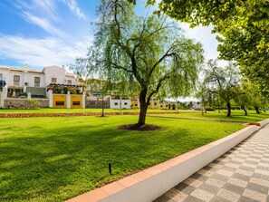 A well-maintained grassy area with a tree in the center, surrounded by a low stone wall and a paved walkway. - 1021 Apartment Morasol (Nerja)
