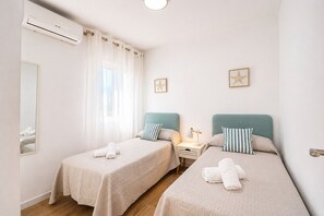 A hotel room with two single beds, a nightstand with a lamp, a mirror, and an air conditioning unit. - 1021 Apartment Morasol (Nerja)