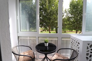 Una habitación con vista a árboles a través de ventanas amplias, una mesita con planta en maceta y dos sillones de mimbre con cojines.