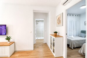Habitación de hotel con cama, mesita de noche con planta, televisor y vista al pasillo.