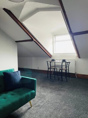 A room with a green sofa, a dining table with chairs, and a window with blinds. - Seafront Comfort Apt | Free WiFi & Parking (Kirkley)