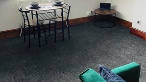 Un comedor con una mesa y sillas, una computadora portátil sobre una mesita y una ventana con persianas.