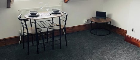 Un comedor con una mesa y sillas, una computadora portátil sobre una mesita y una ventana con persianas.