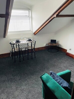 Un comedor con una mesa y sillas, una computadora portátil sobre una mesita y una ventana con persianas.