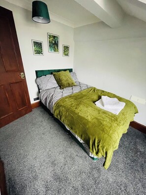 A bedroom with a bed, a door, and a wall-mounted light fixture. - Seafront Comfort Apt | Free WiFi & Parking (Kirkley)