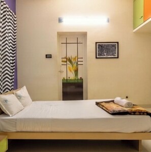 A single bed with a headboard, a bedside table, a nightstand, a framed picture on the wall, and a door with a decorative panel. - Hotel Bright stays (Thiruvananthapuram)