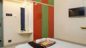 Quarto com cama, televisão na parede e guarda-roupa com portas vermelhas e verdes.