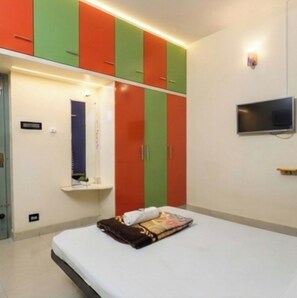 A bedroom with a bed, a TV mounted on the wall, and a wardrobe with red and green doors. - Hotel Bright stays (Thiruvananthapuram)